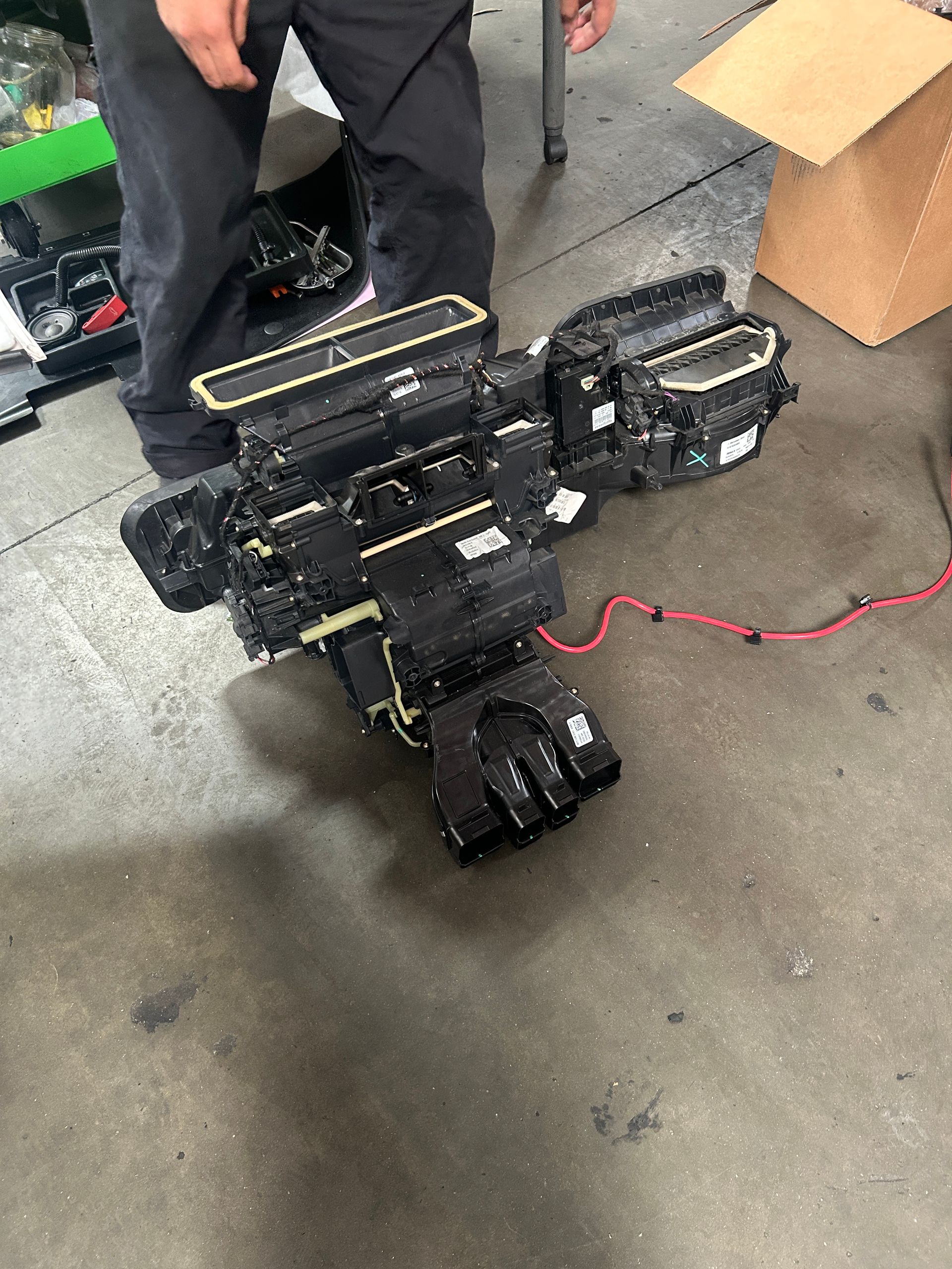 Scattered black camera equipment on wet pavement beside a person's legs and an open cardboard box