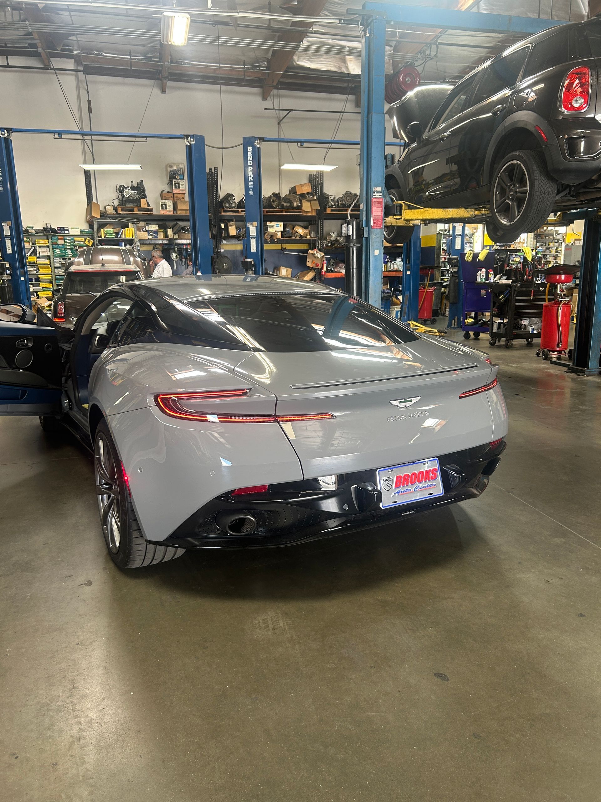 Gray convertible sports car in an auto shop, viewed from the rear with other vehicles on lifts nearby