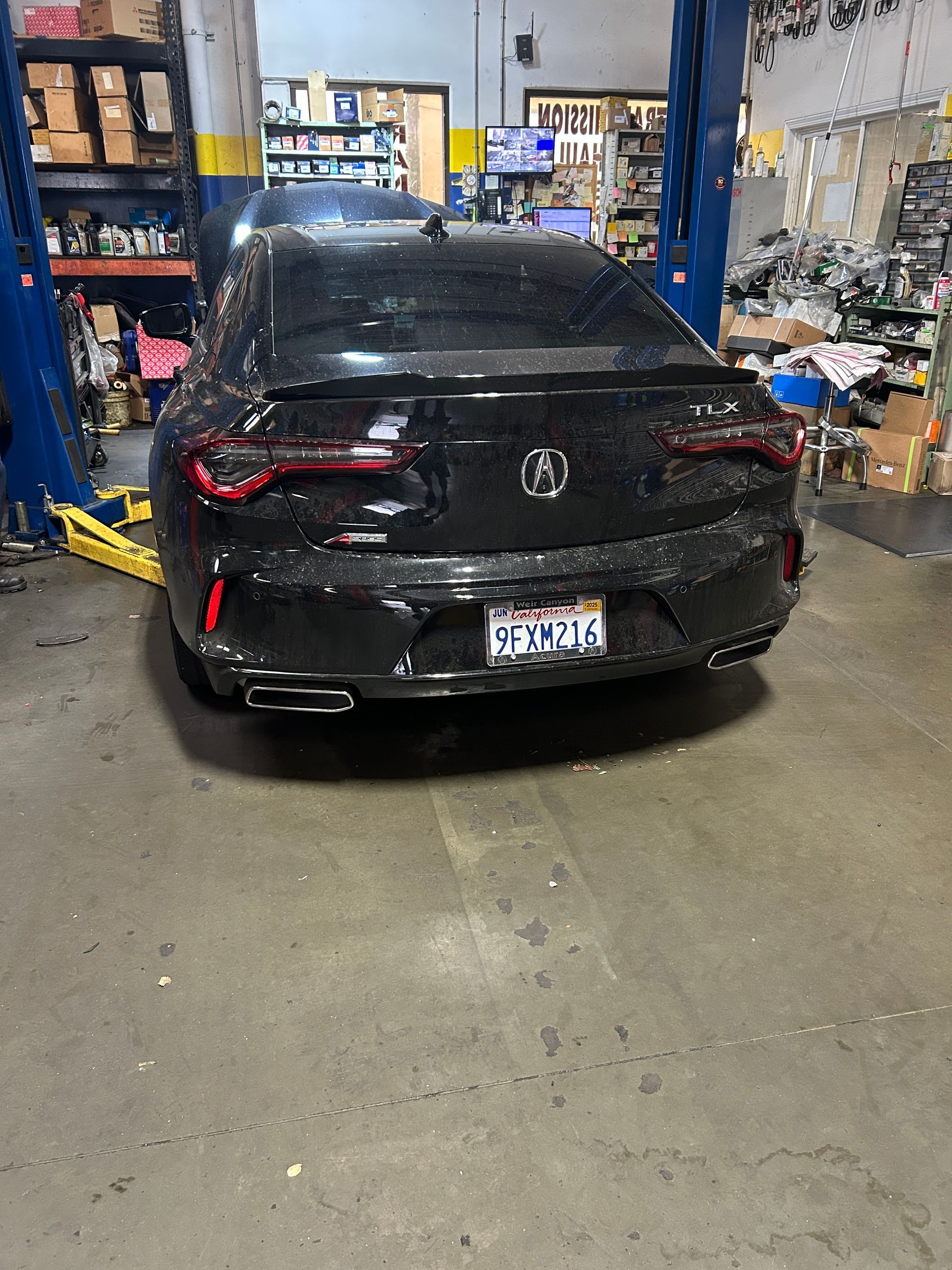 Black Acura sedan on a car lift in an auto repair shop.