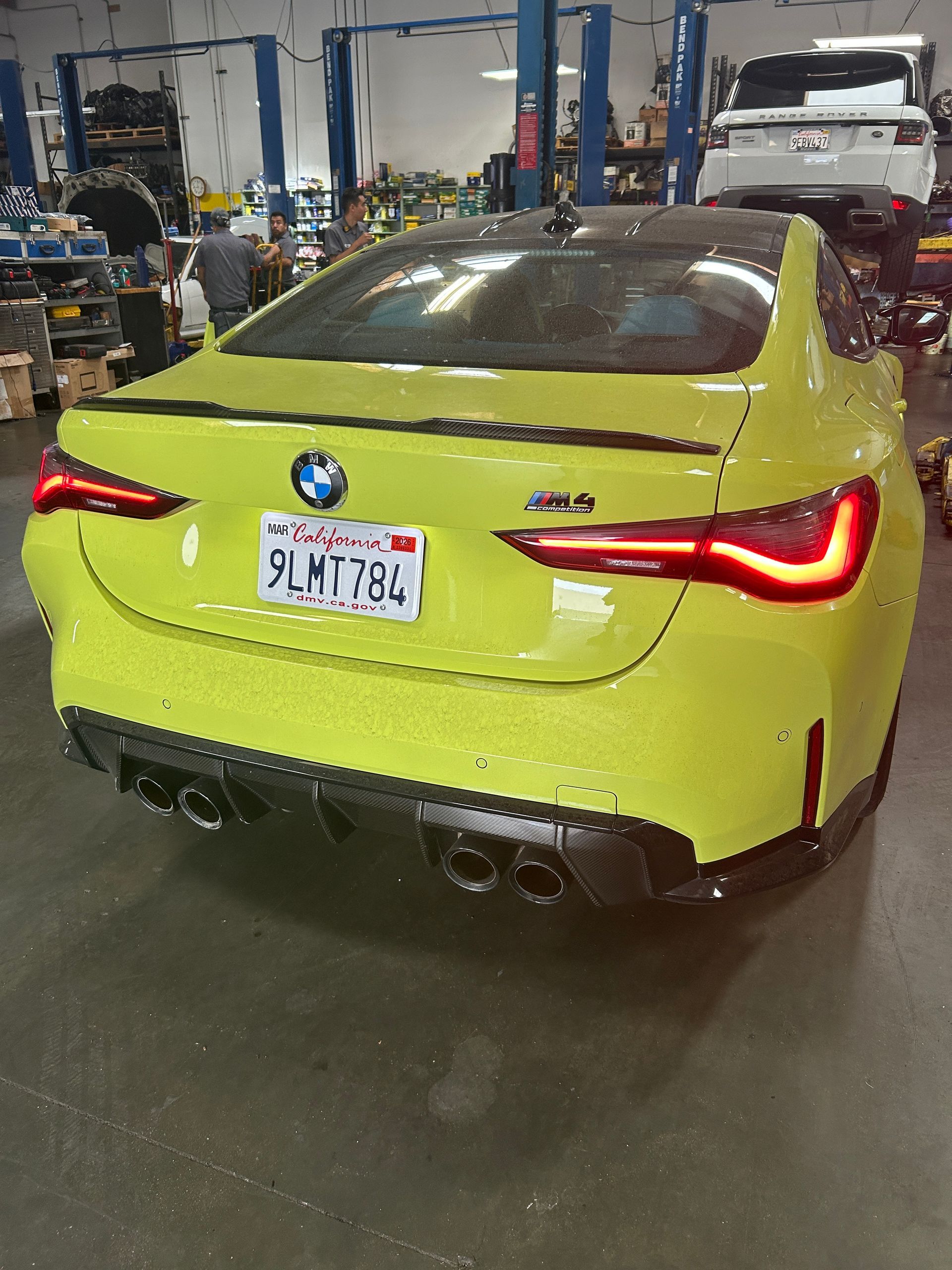 Yellow BMW coupe in a garage, rear view with taillights lit and California license plate.