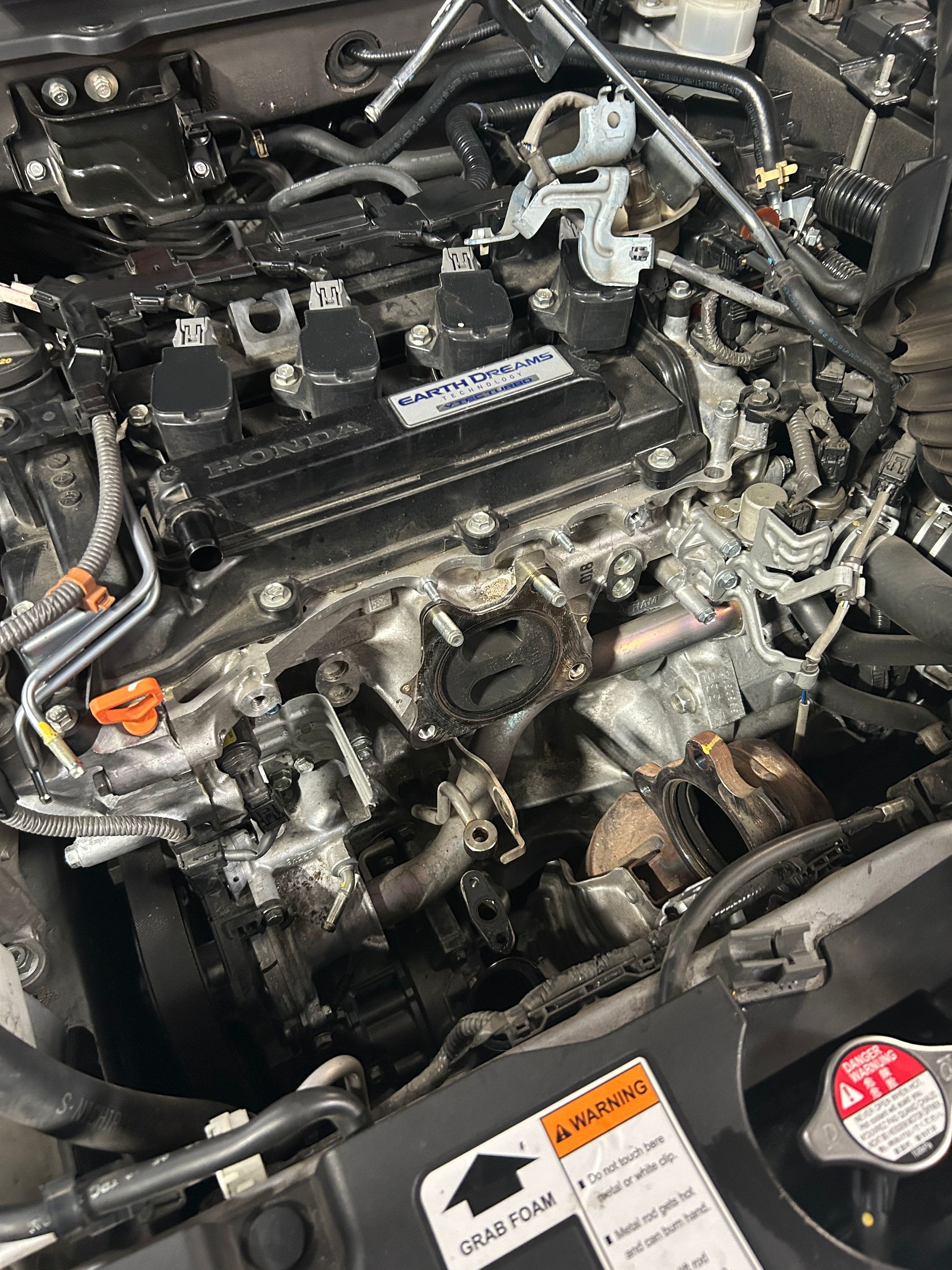 Close-up of a car engine bay with hoses, wiring, and a radiator cap visible.
