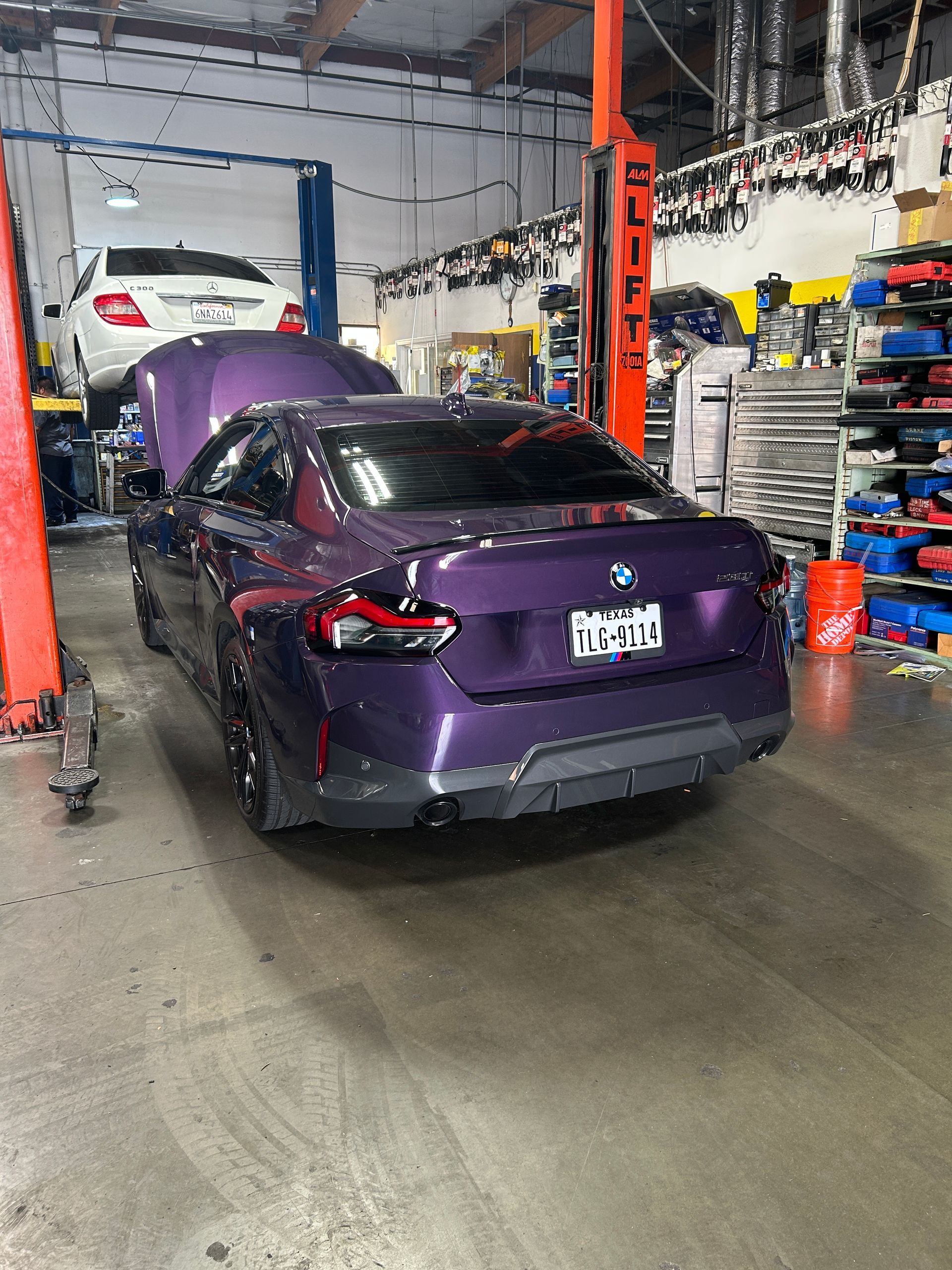 Purple sedan in an auto repair shop bay, with lifts, tools, and equipment around it.
