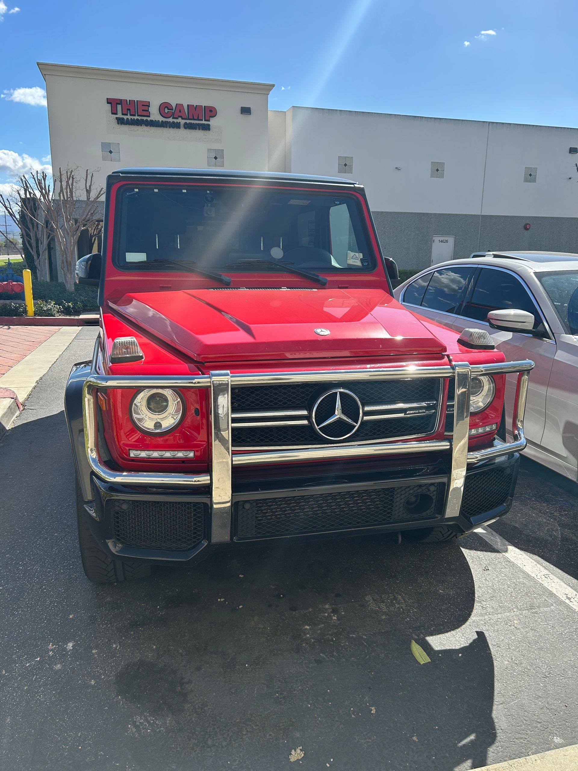 Red Mercedes G-Class SUV parked in a lot outside a building under bright sunlight