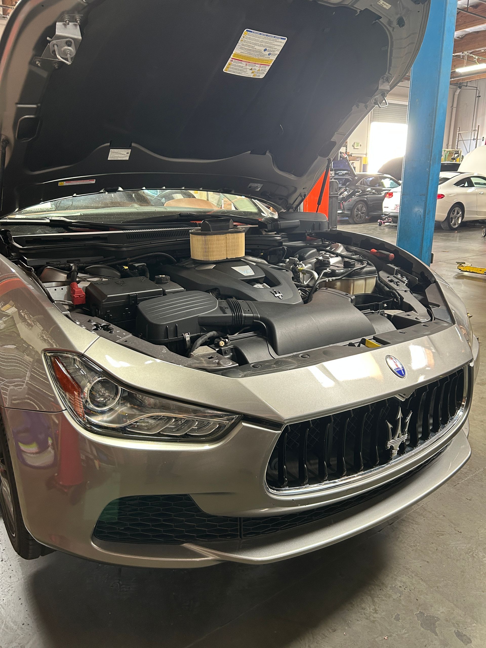 Silver car with hood open in a garage, showing engine bay and front grille.