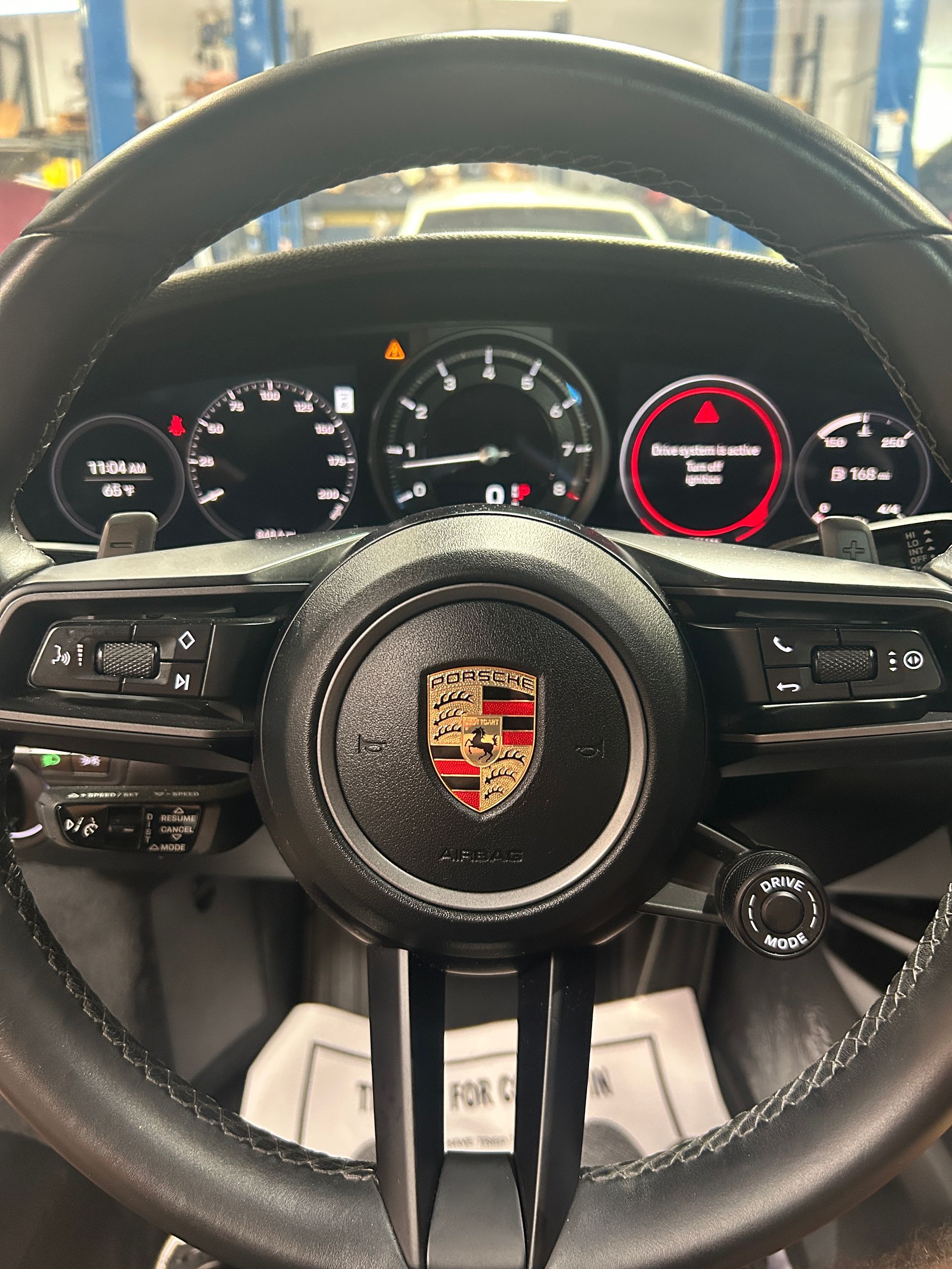 Porsche steering wheel and instrument cluster inside a sports car, with illuminated gauges and central tachometer.