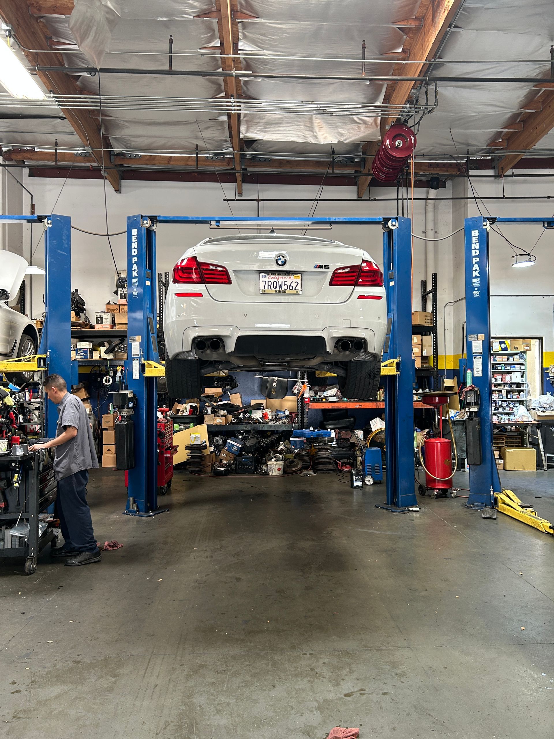 White sedan on a lift in an auto repair shop with blue posts and tools in the background