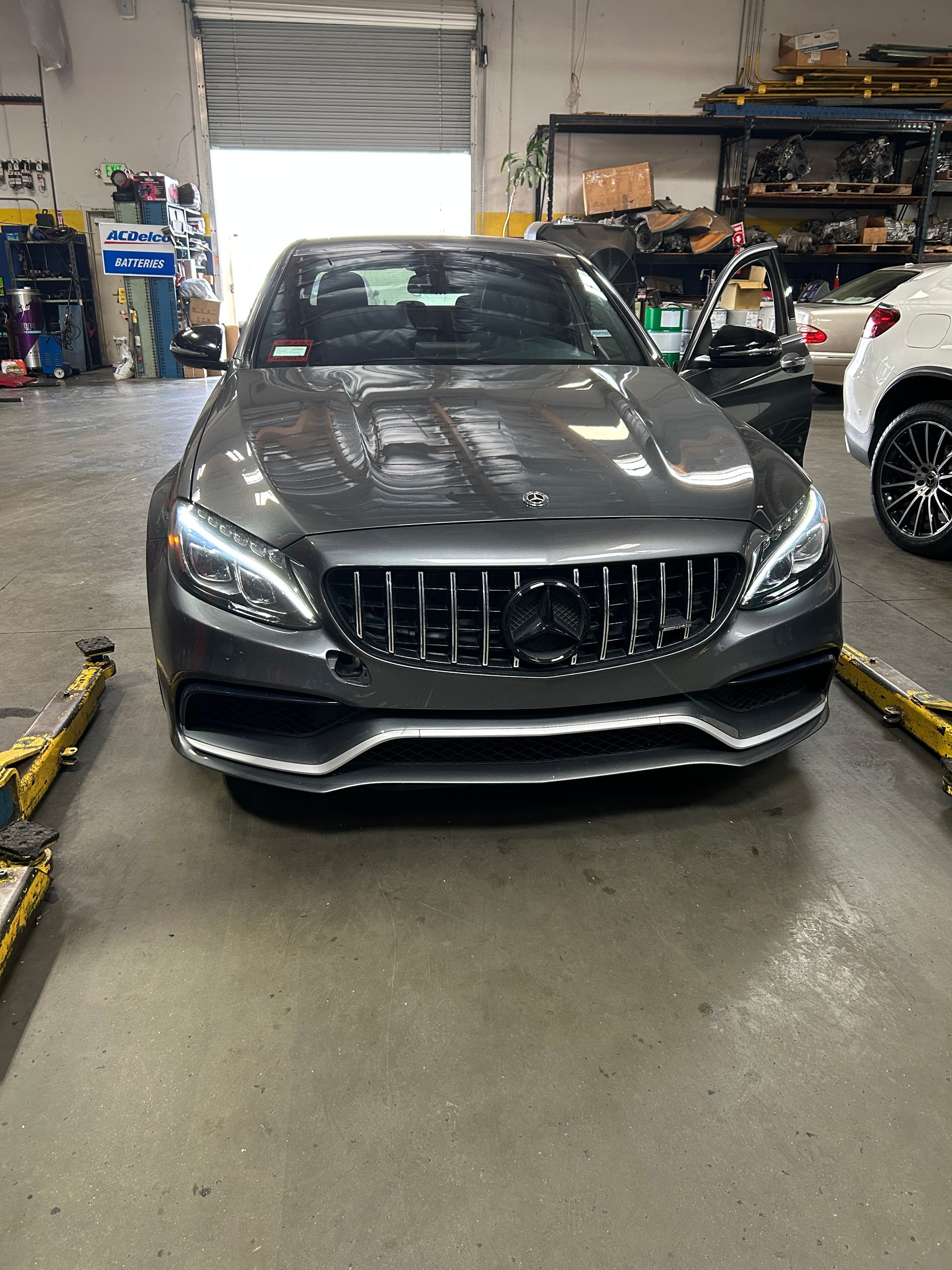 Gray Mercedes-Benz sedan in a workshop, front view with garage equipment and cars in the background
