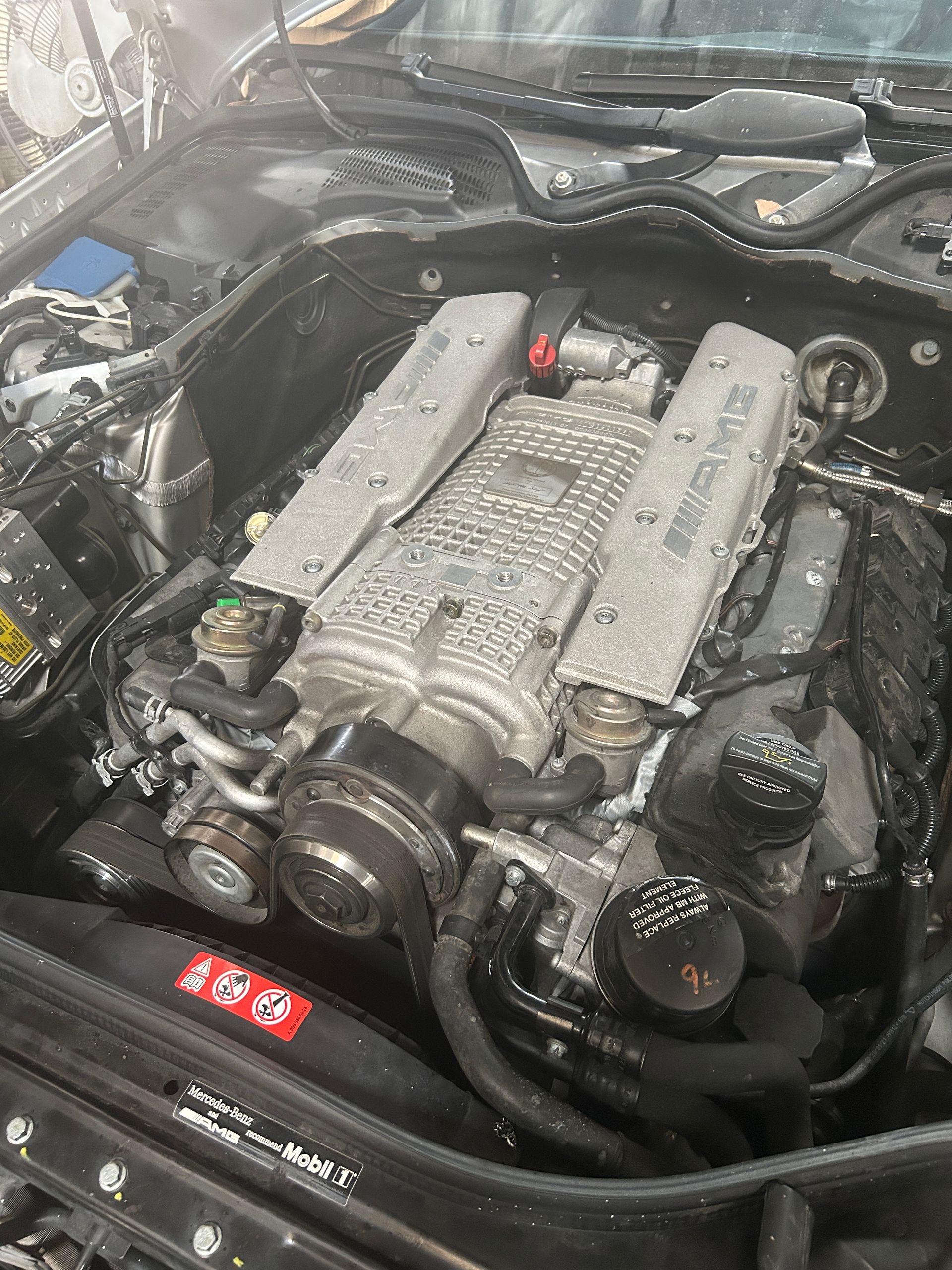 Close-up of a car engine bay with a silver engine cover and black hoses under the hood