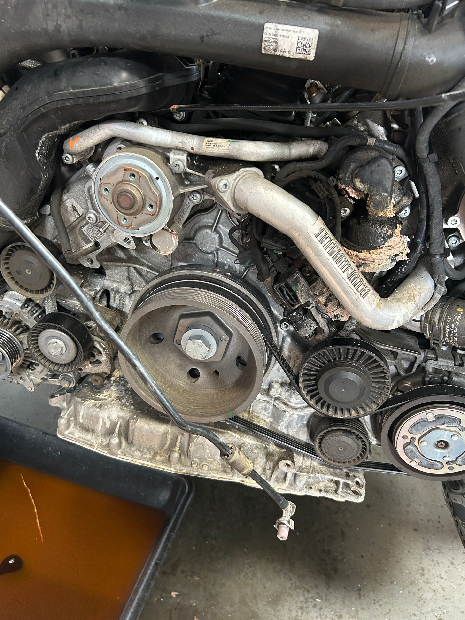 Close-up of a disassembled engine with belts, pulleys, hoses, and greasy metal parts.