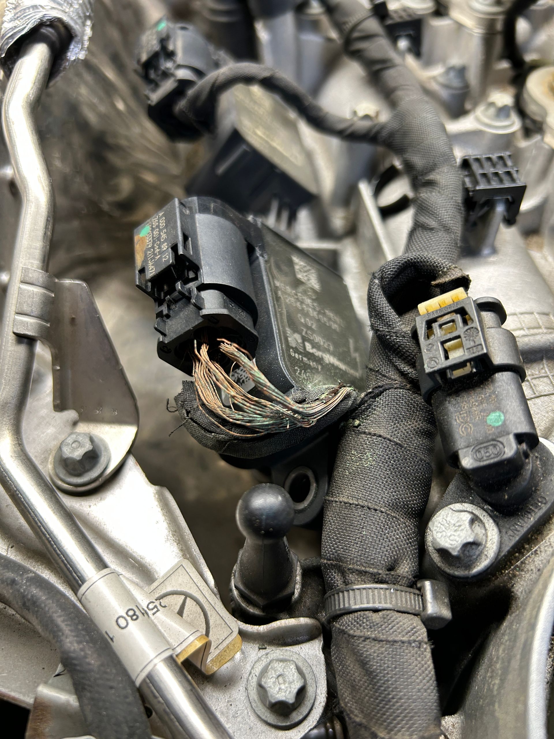 Damaged wiring harness and connectors inside a car engine bay with exposed copper wires
