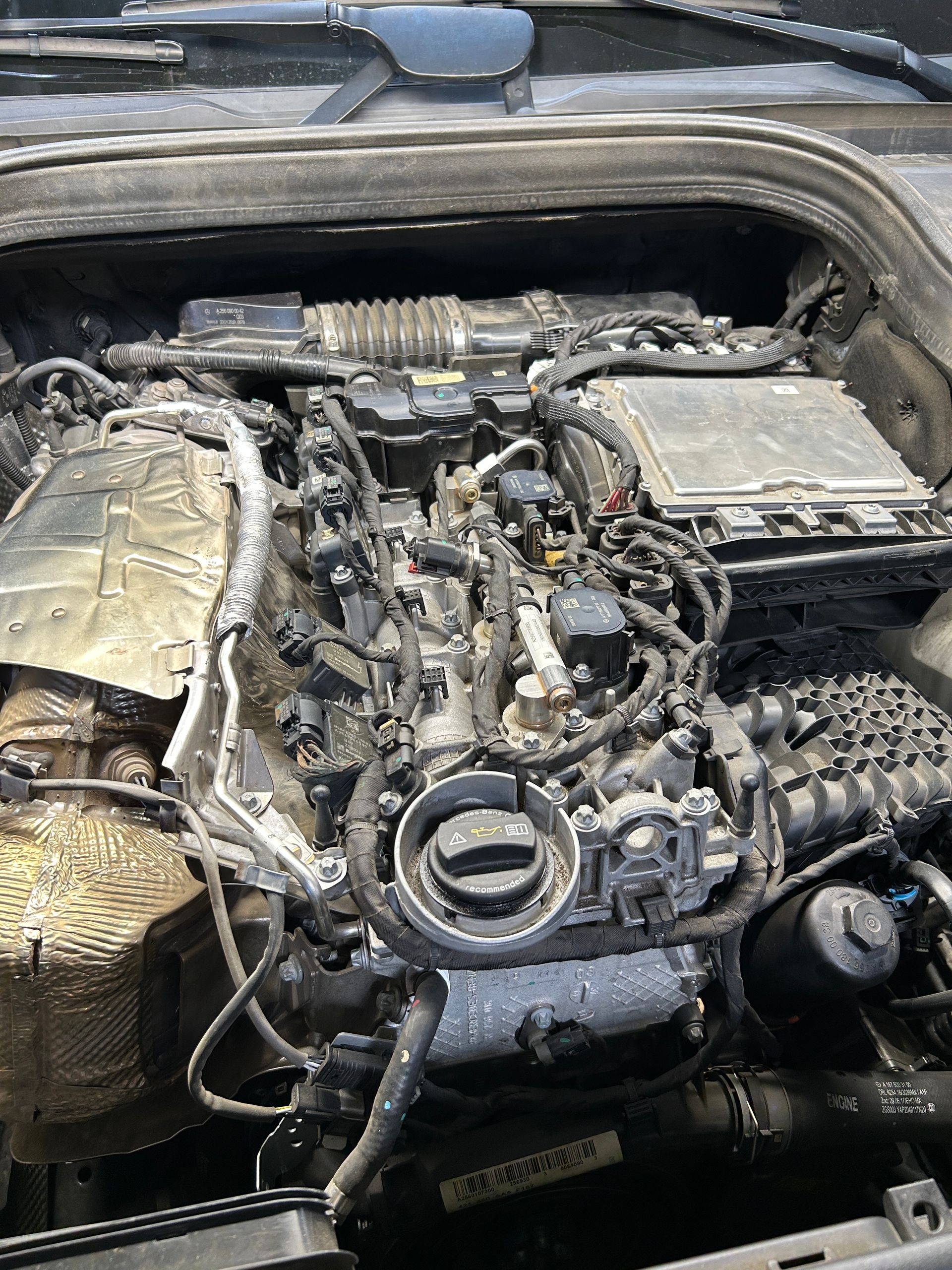 Engine bay of a car with exposed parts, hoses, and a dusty engine cover under the hood.