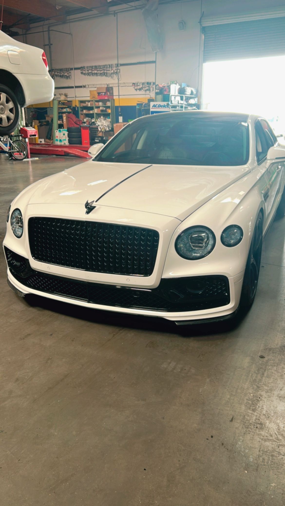 White Bentley coupe in a garage workshop, front view.