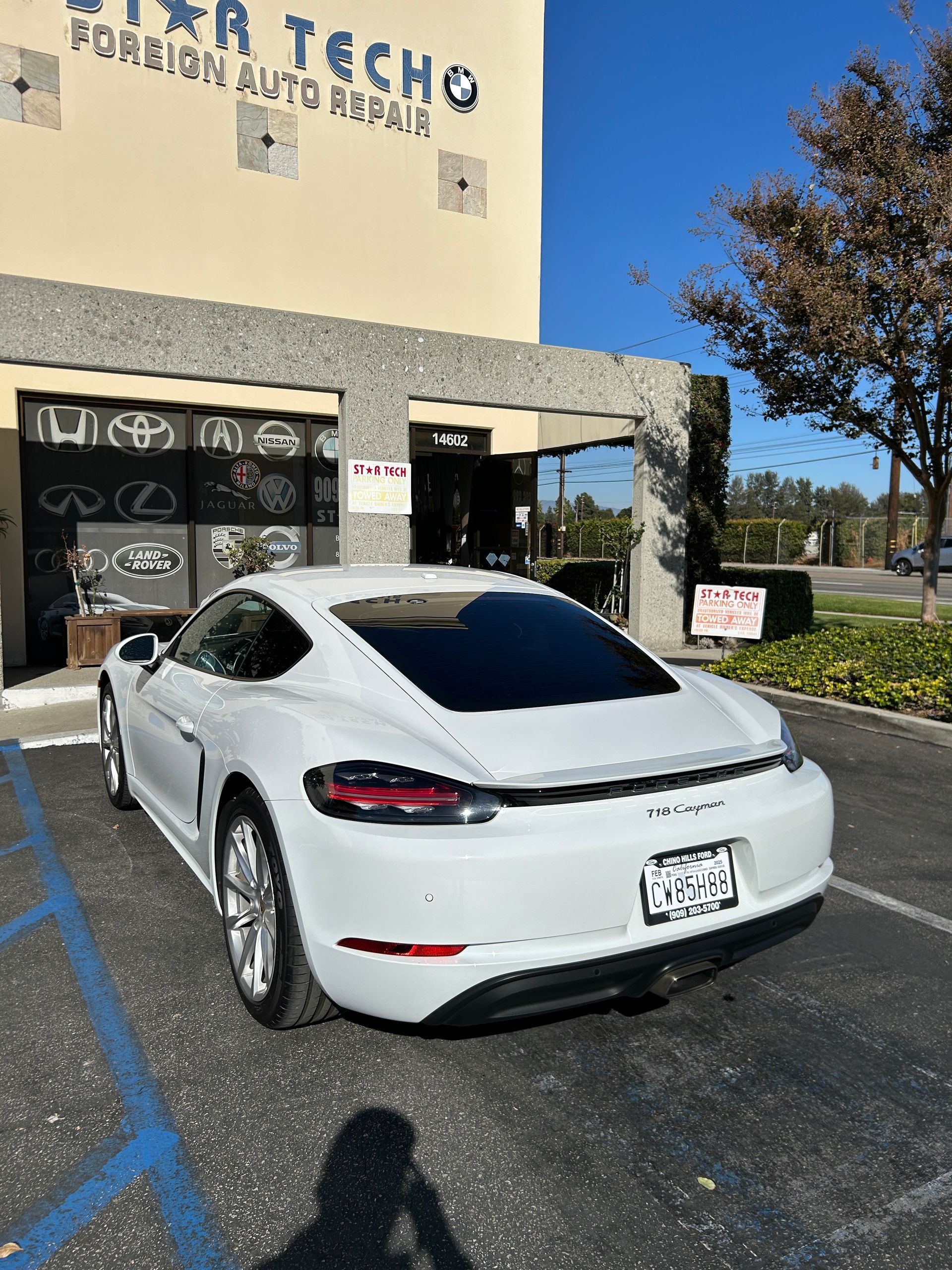 White Tesla parked outside a building entrance with “Techno” signage and a handicapped parking spot nearby
