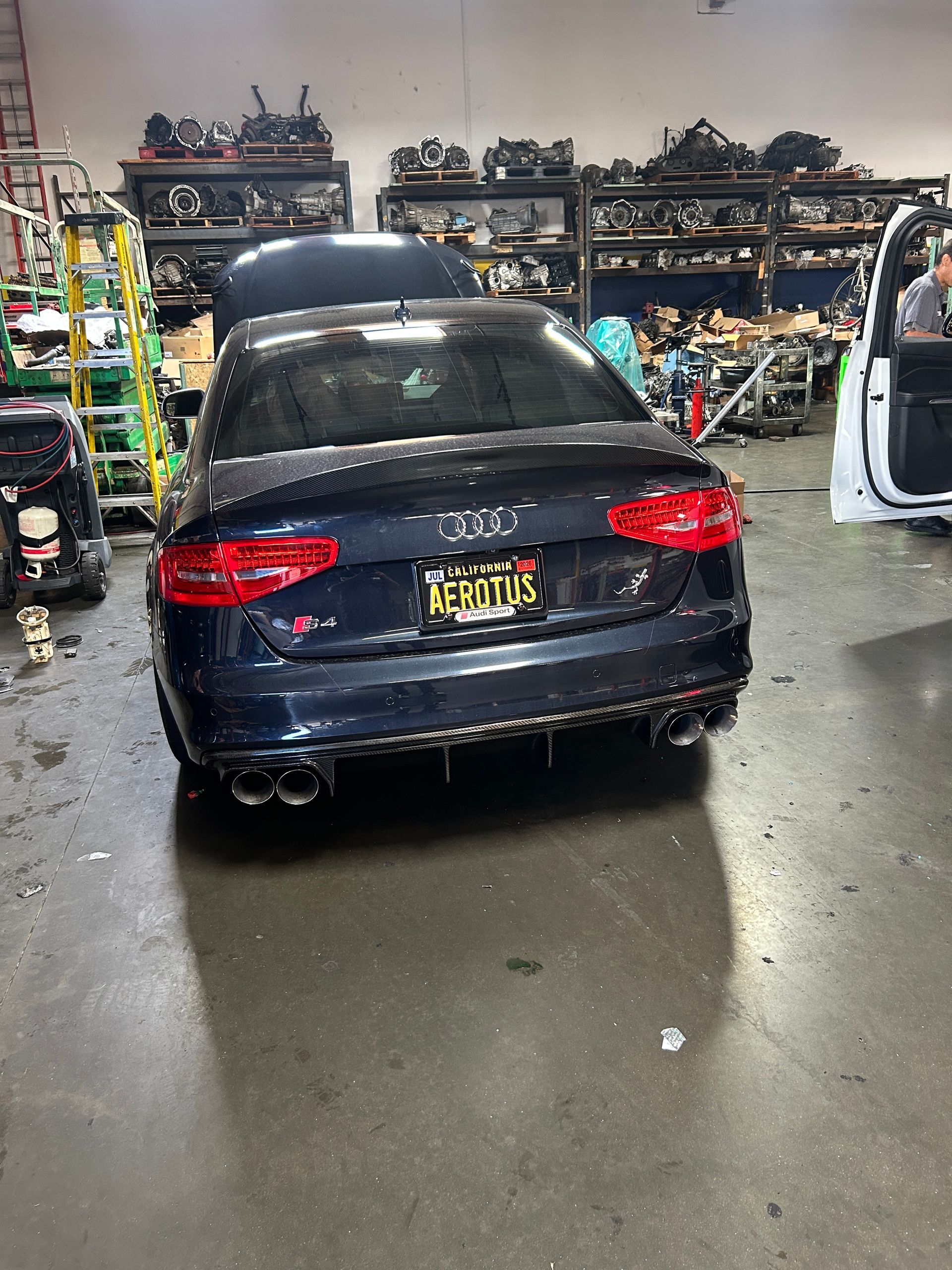 Dark blue Audi sedan in a cluttered auto repair shop with shelves of parts in the background