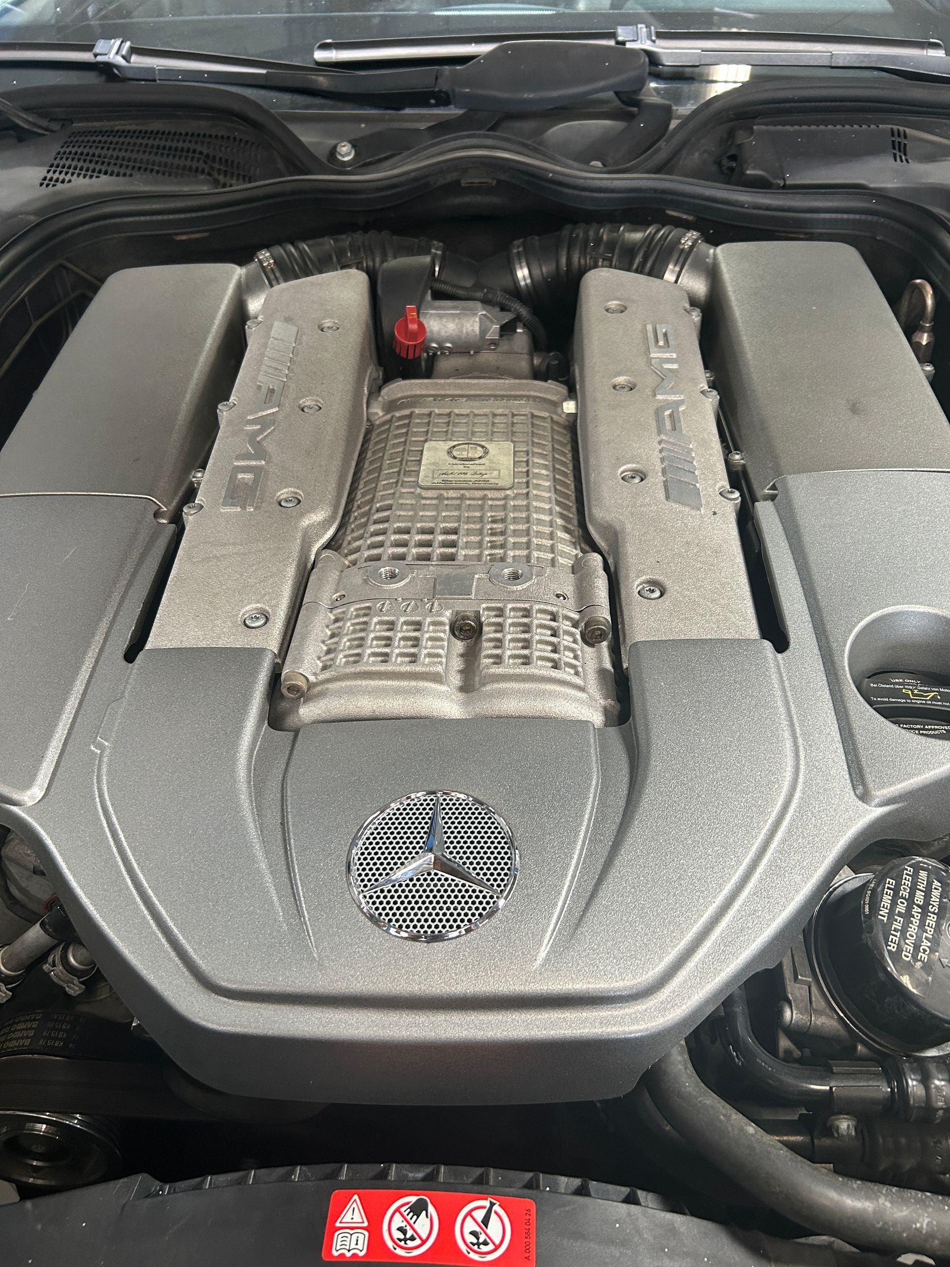 Dusty car engine compartment with a black engine cover and red warning labels