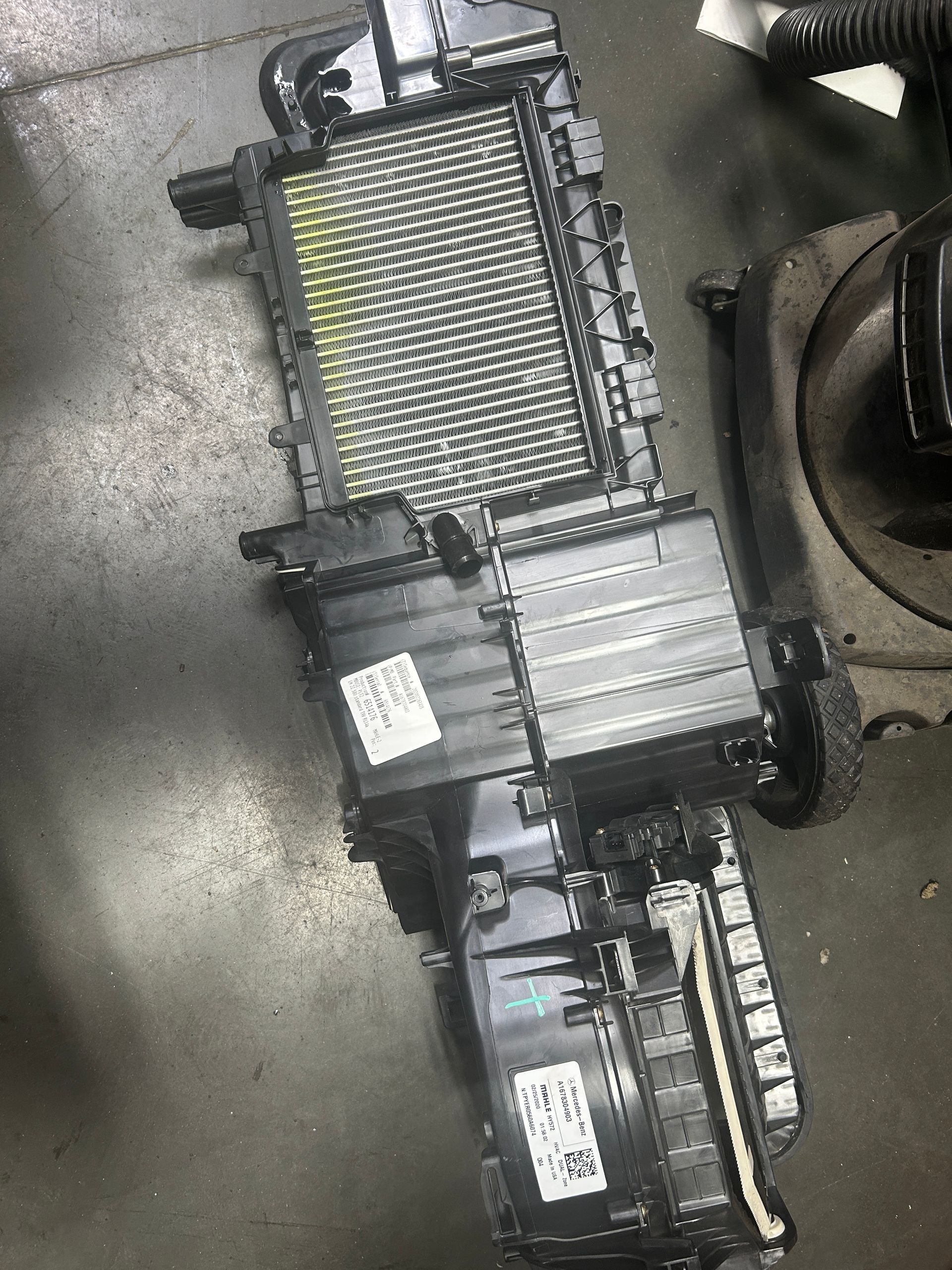 Automotive parts on a floor: a silver radiator, black motor assembly, and electronic modules.