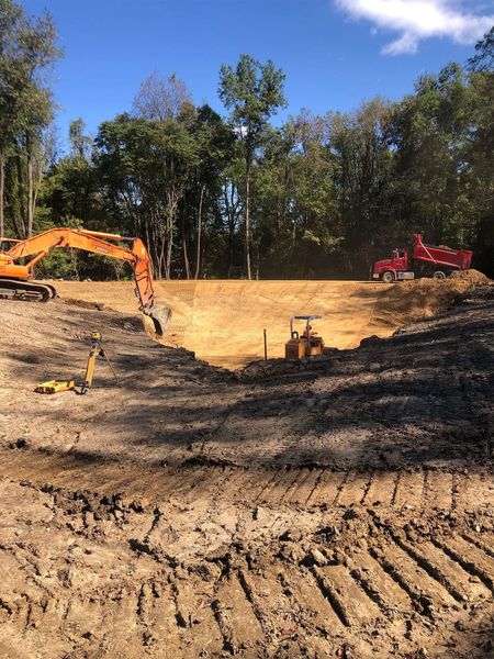 Construction site: Excavators, bulldozer, and dump truck on earth, trees in background, clear sky.