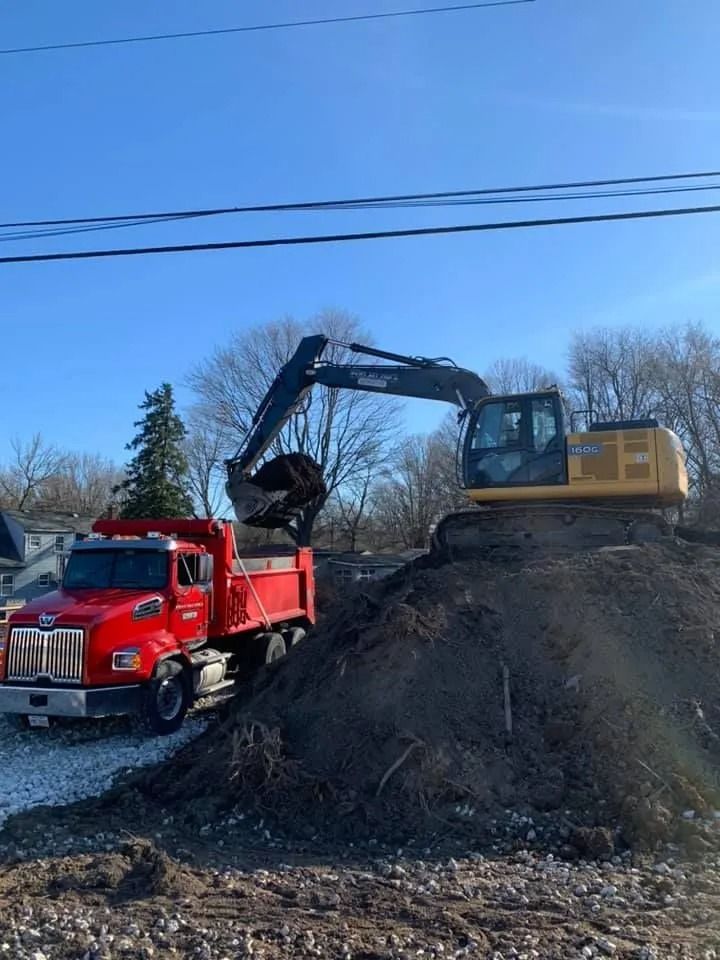 A yellow excavator loads dirt into a red dump truck under a clear blue sky.
