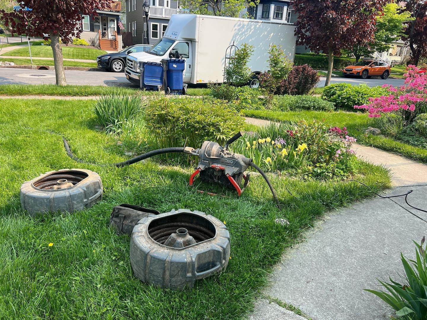 A residential lawn features two tire planters and a gas-powered lawn edger in front of a parked moving truck.