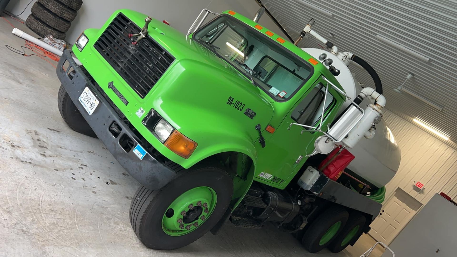 A bright green tanker truck parked inside a bright, clean garage facility.