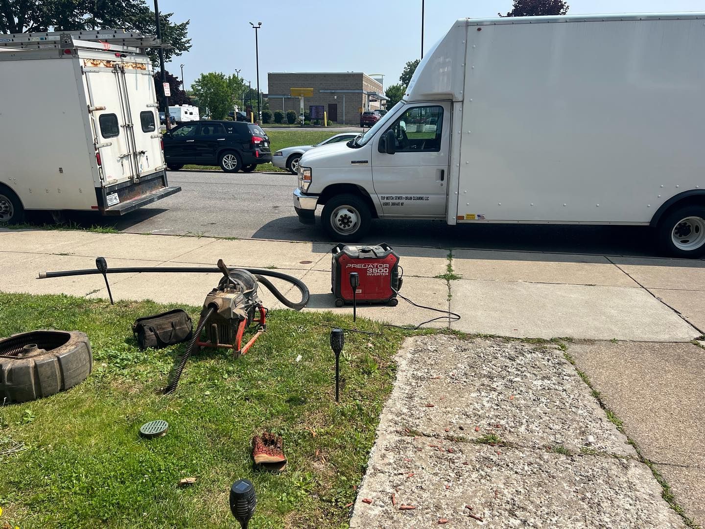 A red generator powers equipment on a grassy area next to two parked utility trucks on a concrete lot.