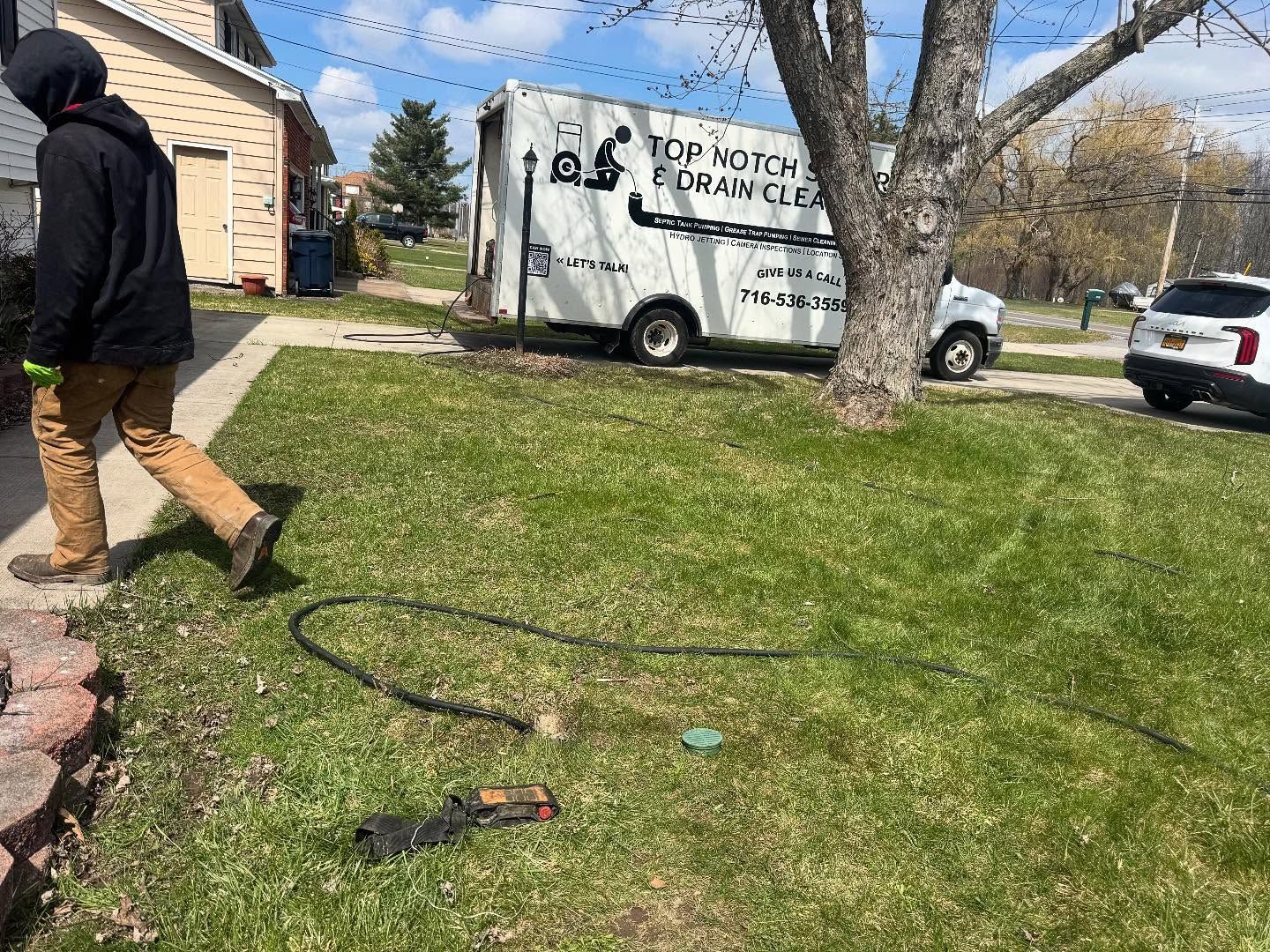 A person in a black hoodie and tan pants walks across a grassy lawn near a white utility truck and a parked car.