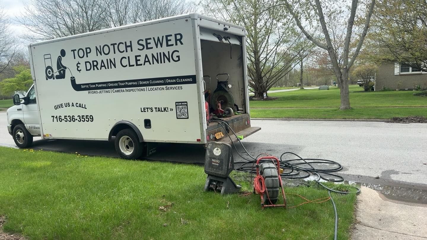 A Top Notch Sewer & Drain Cleaning truck parked on a residential street with drain cleaning equipment on the lawn.