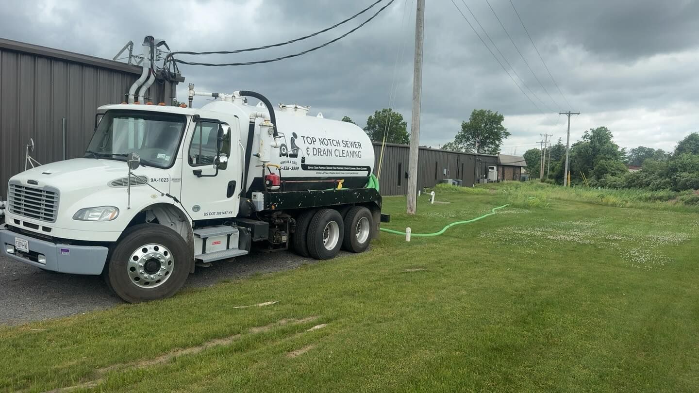 A white utility vacuum truck parked on a grass lawn next to a building on a cloudy day.