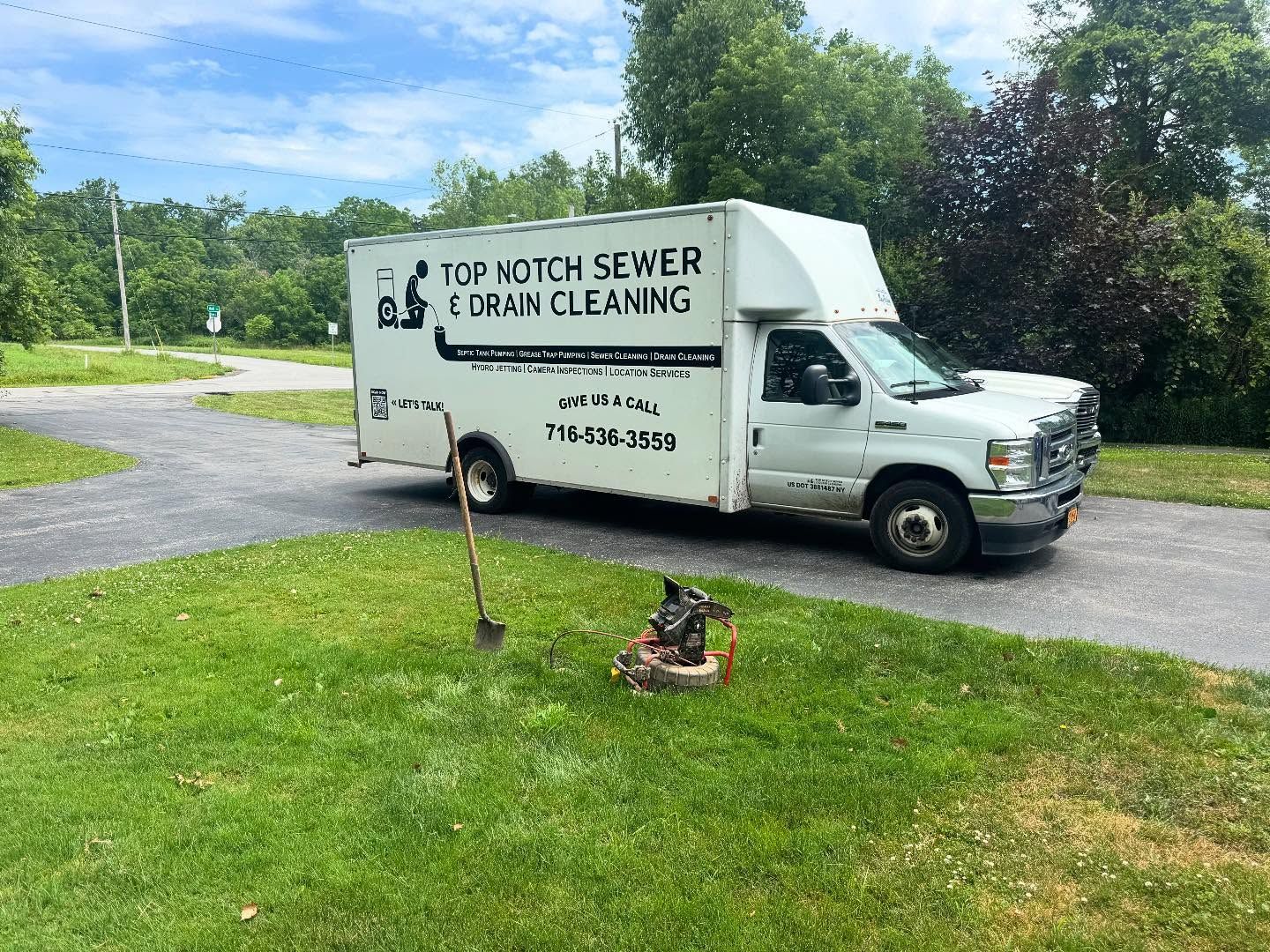 A white Top Notch Sewer & Drain Cleaning truck parked on a gravel driveway near a grass lawn with equipment.
