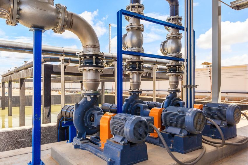 Three industrial water pumps with blue motors and metal piping sit on a concrete pad under a partly cloudy sky.