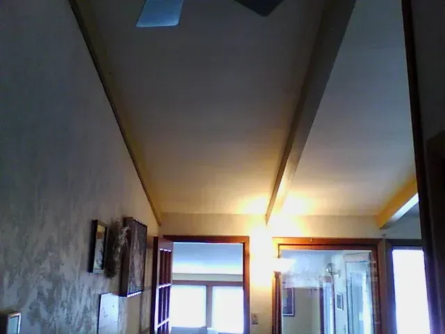 Ceiling of a room, with beams and doorways, lit by ambient lighting.