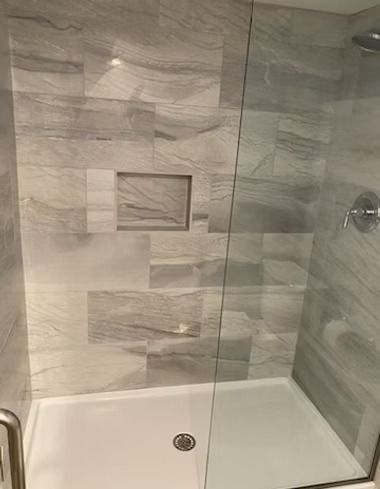 A tiled walk-in shower with a glass panel, a built-in recessed shelf, and silver fixtures.