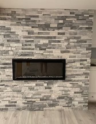 A linear, black-framed electric fireplace is mounted on a feature wall covered in gray and white horizontal stone veneer.