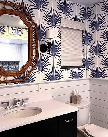 Bathroom vanity with a white sink, bamboo-style mirror, shiplap walls, and bold palm-leaf patterned wallpaper.