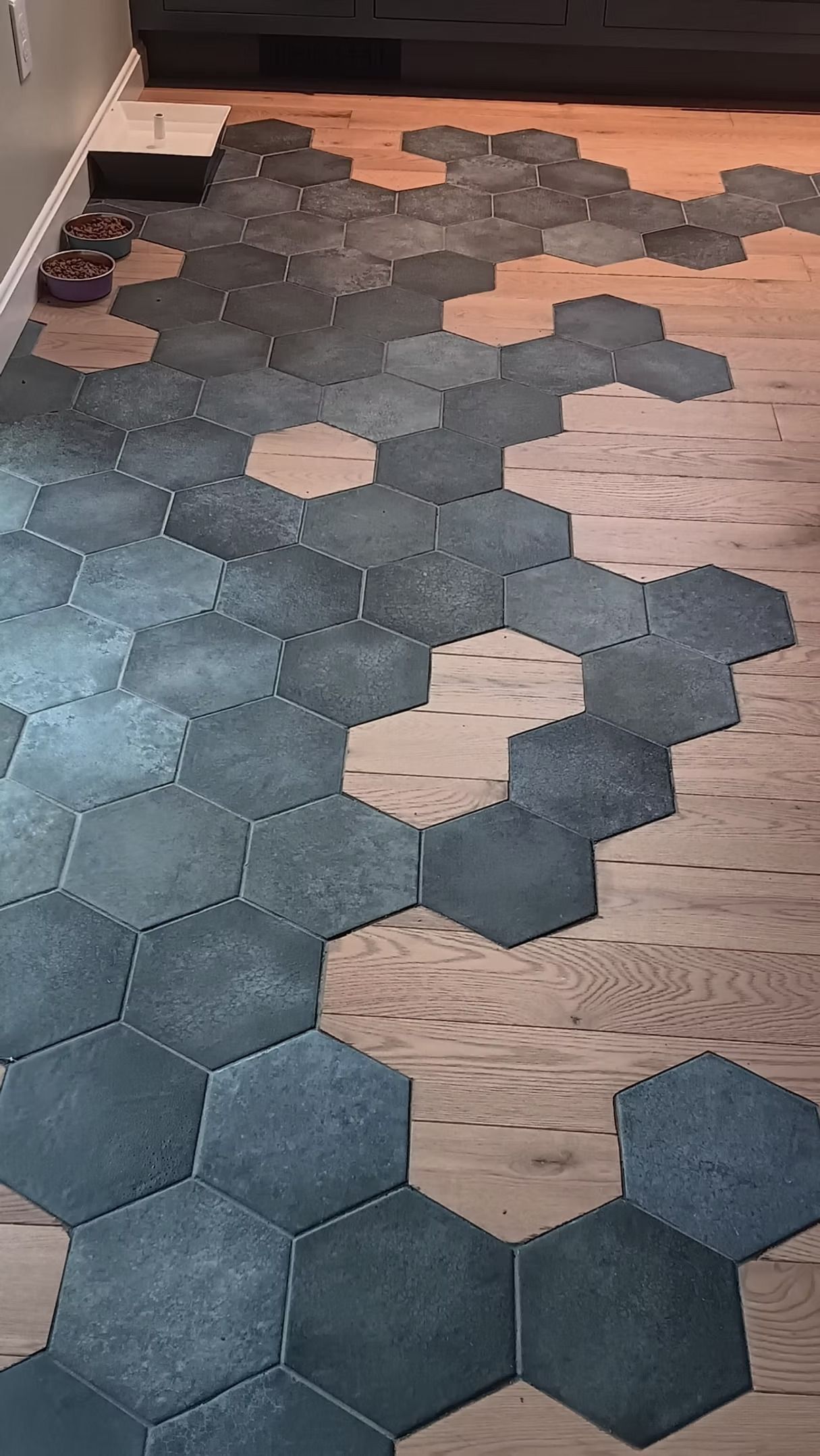 A section of wood floor partially covered by a scattered, irregular pattern of grey hexagonal felt tiles.