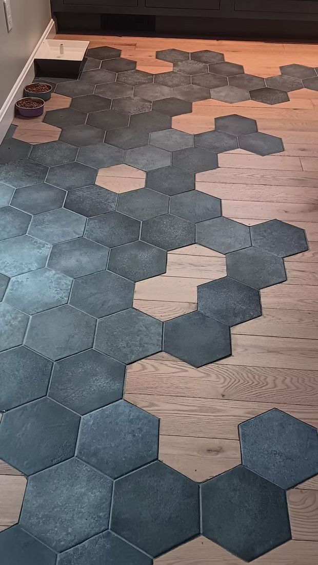 A room floor with a gradient pattern of interlocking dark grey hexagonal tiles transitioning into light wood flooring.