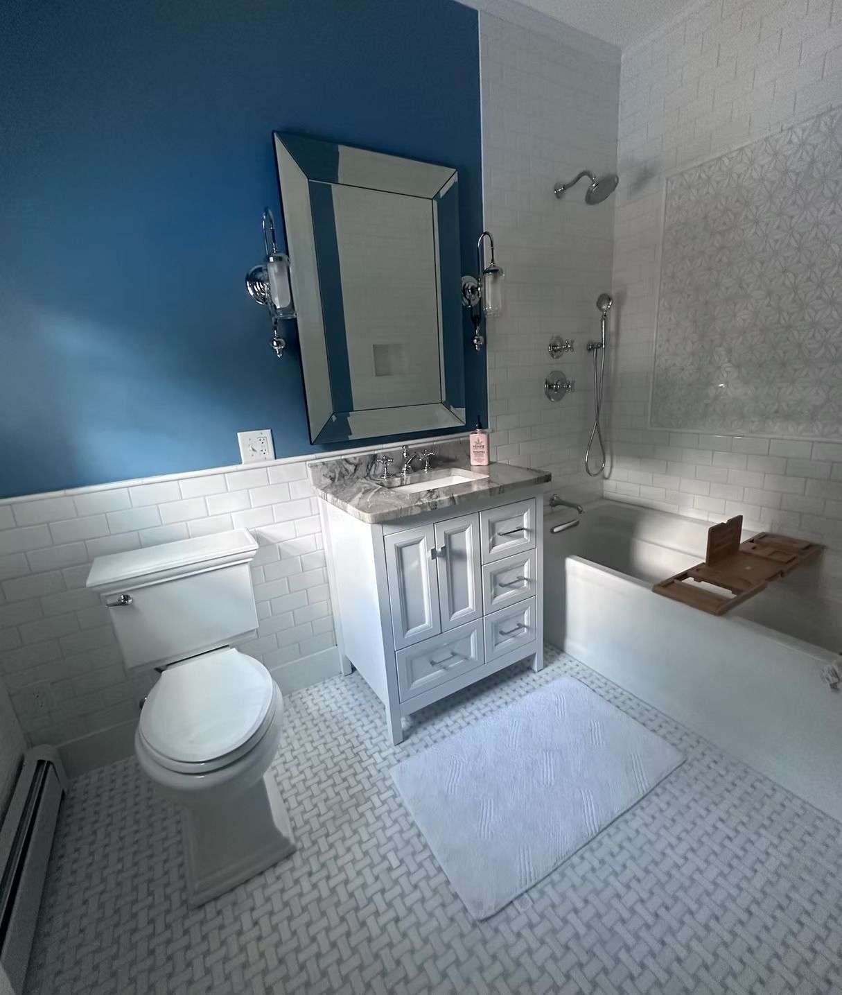 A bathroom with a white vanity, a blue accent wall, a mirror, a toilet, and a bathtub with white tile walls and floor.
