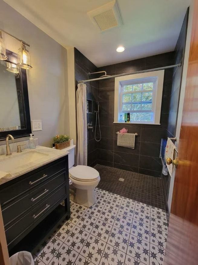 A bathroom with black cabinetry, a patterned tile floor, and a walk-in shower with dark tile and a window.