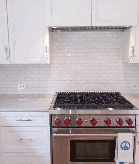 White kitchen with a stainless steel gas range, subway tile backsplash, and light grey countertops.