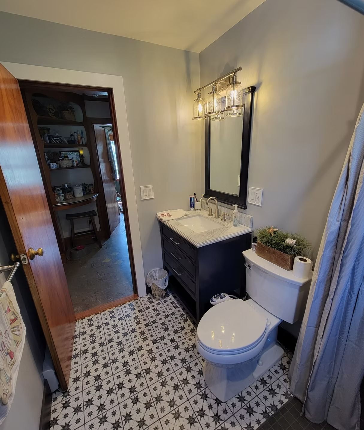 A small bathroom with patterned tile floors, a dark blue vanity, a mirror with light fixtures, and a white toilet.