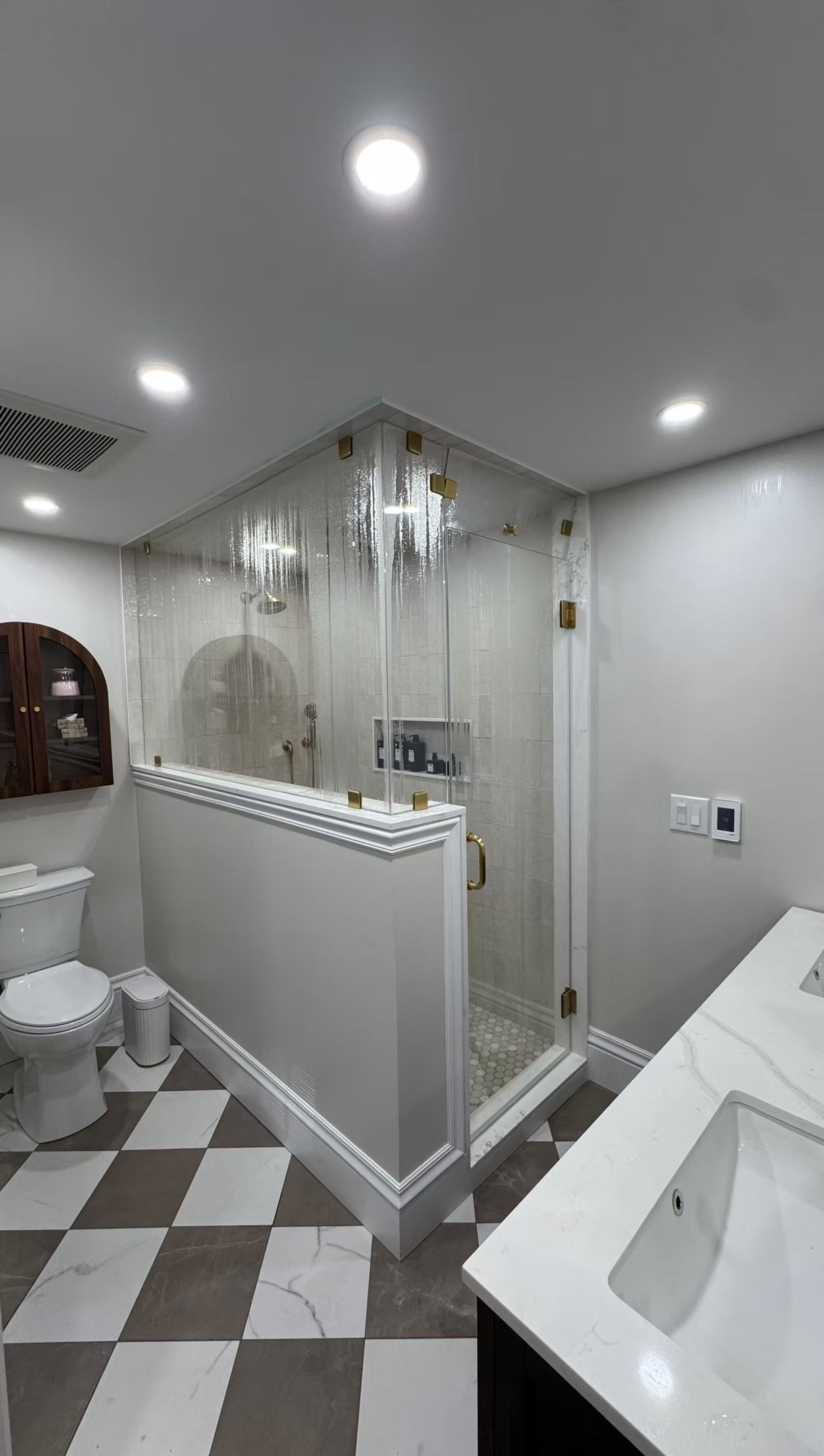 A modern bathroom featuring a checkerboard floor, a toilet, a vanity with a white counter, and a glass-enclosed shower.