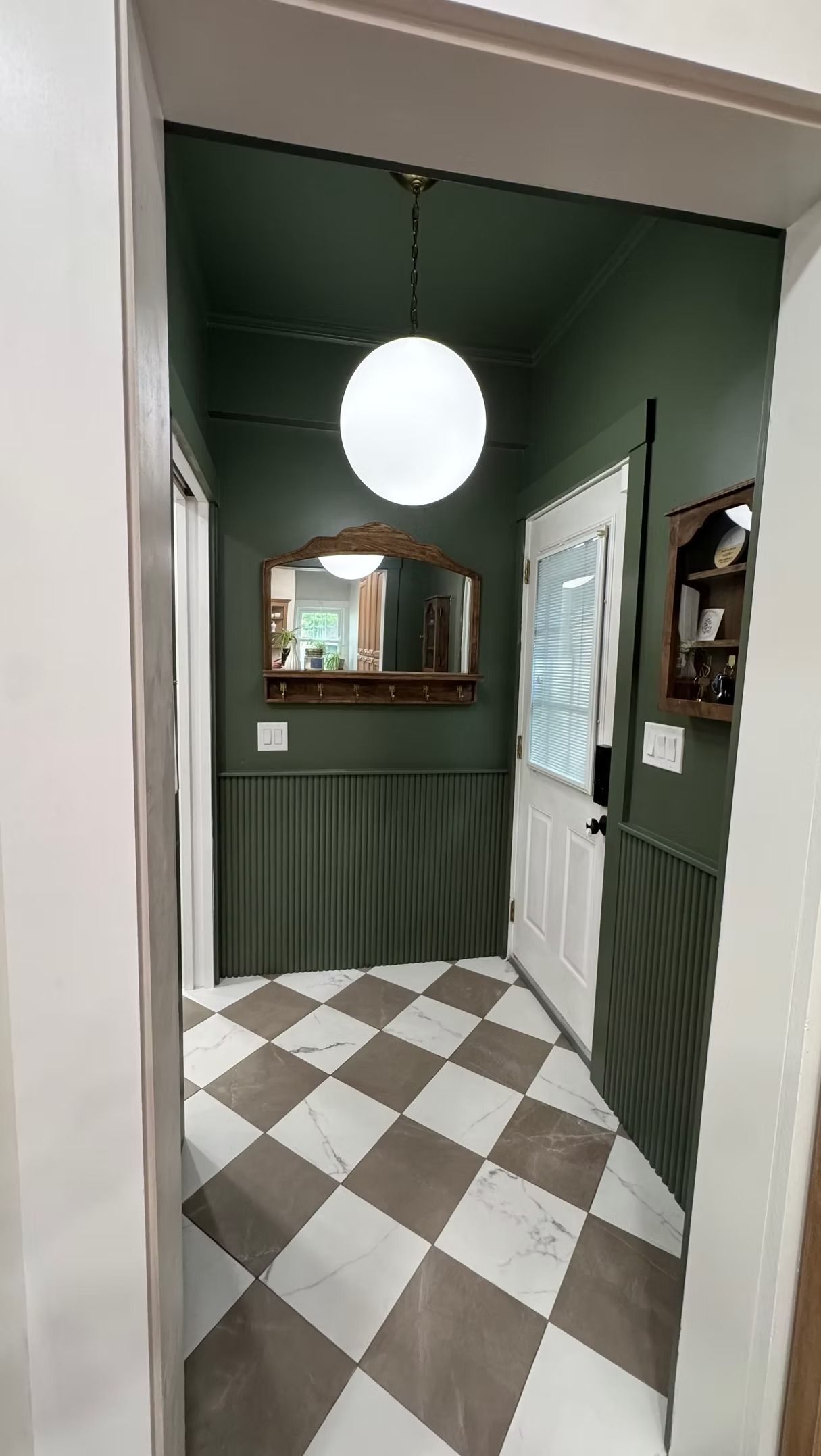 Small bathroom with dark green walls, checkered floor, round ceiling light, sink mirror, and shower curtain.