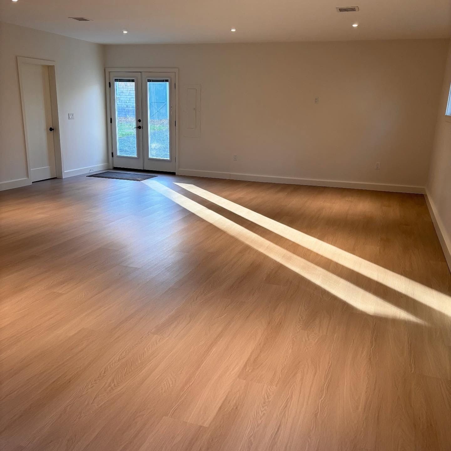An empty room with light wood floors, a door to the left, and glass-paneled double doors leading outside.