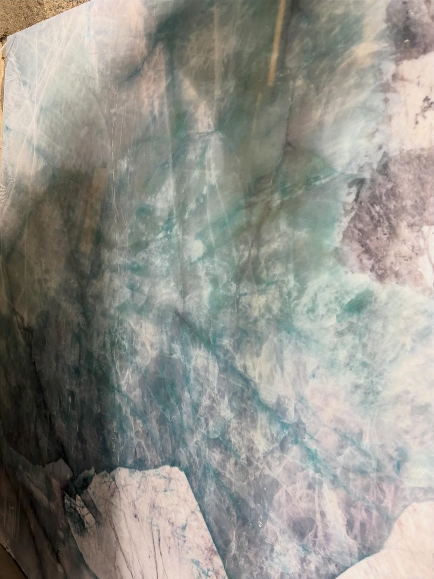 A close-up of marble or stone featuring swirling patterns of white, teal, and soft grey tones.
