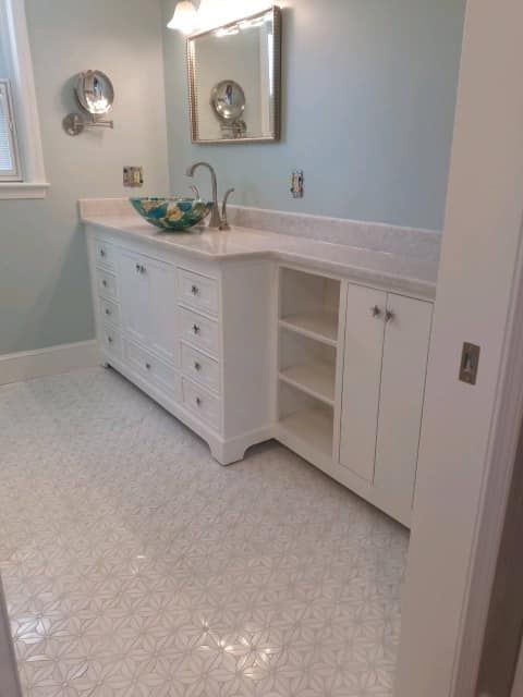 White bathroom vanity with sink, mirror, and light blue walls on a speckled floor.