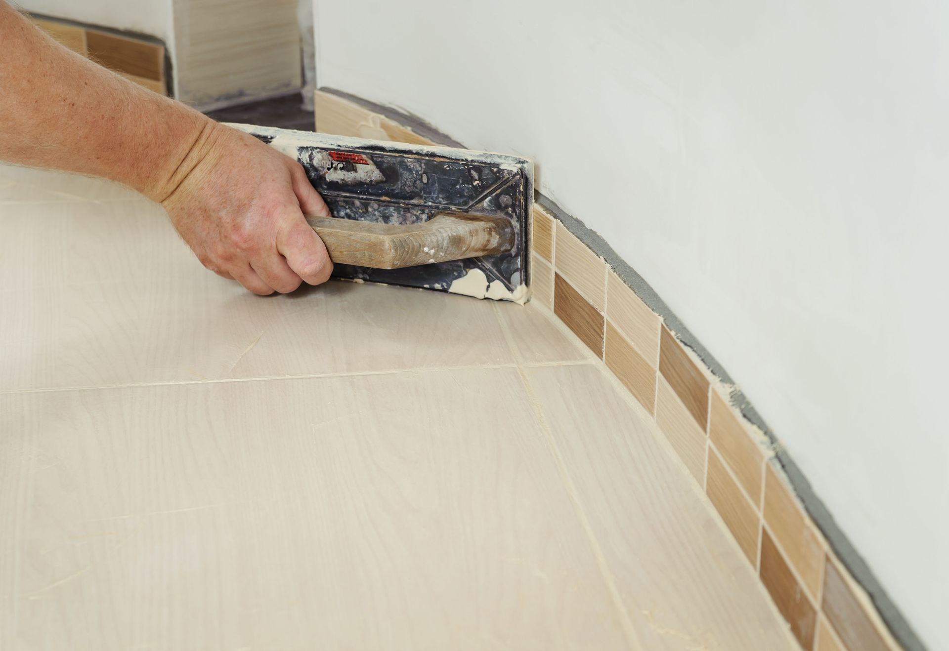 Hand spreading grout on a tiled wall edge with a trowel indoors