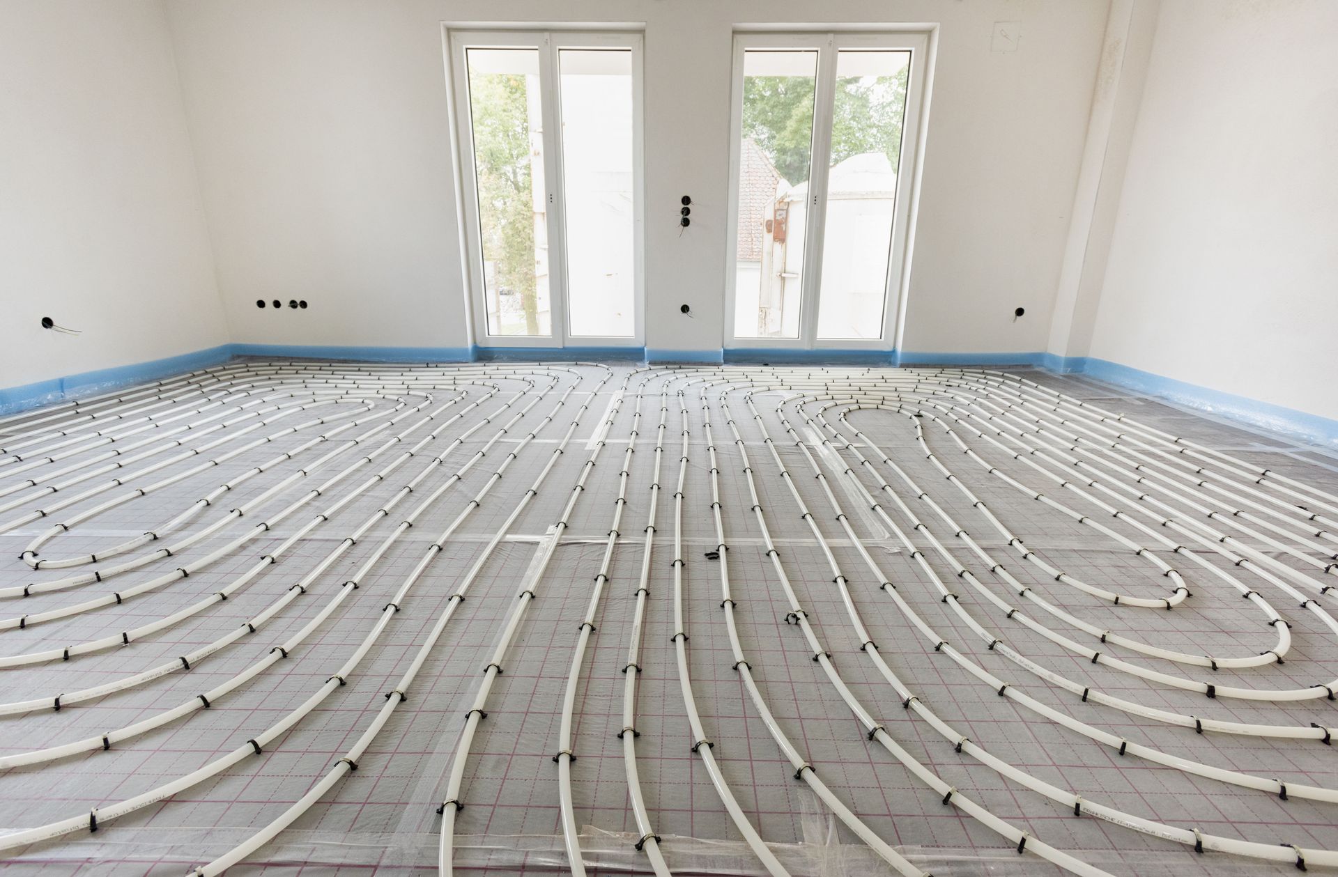 Empty room with underfloor heating pipes laid over concrete, white walls, and glass doors at the back