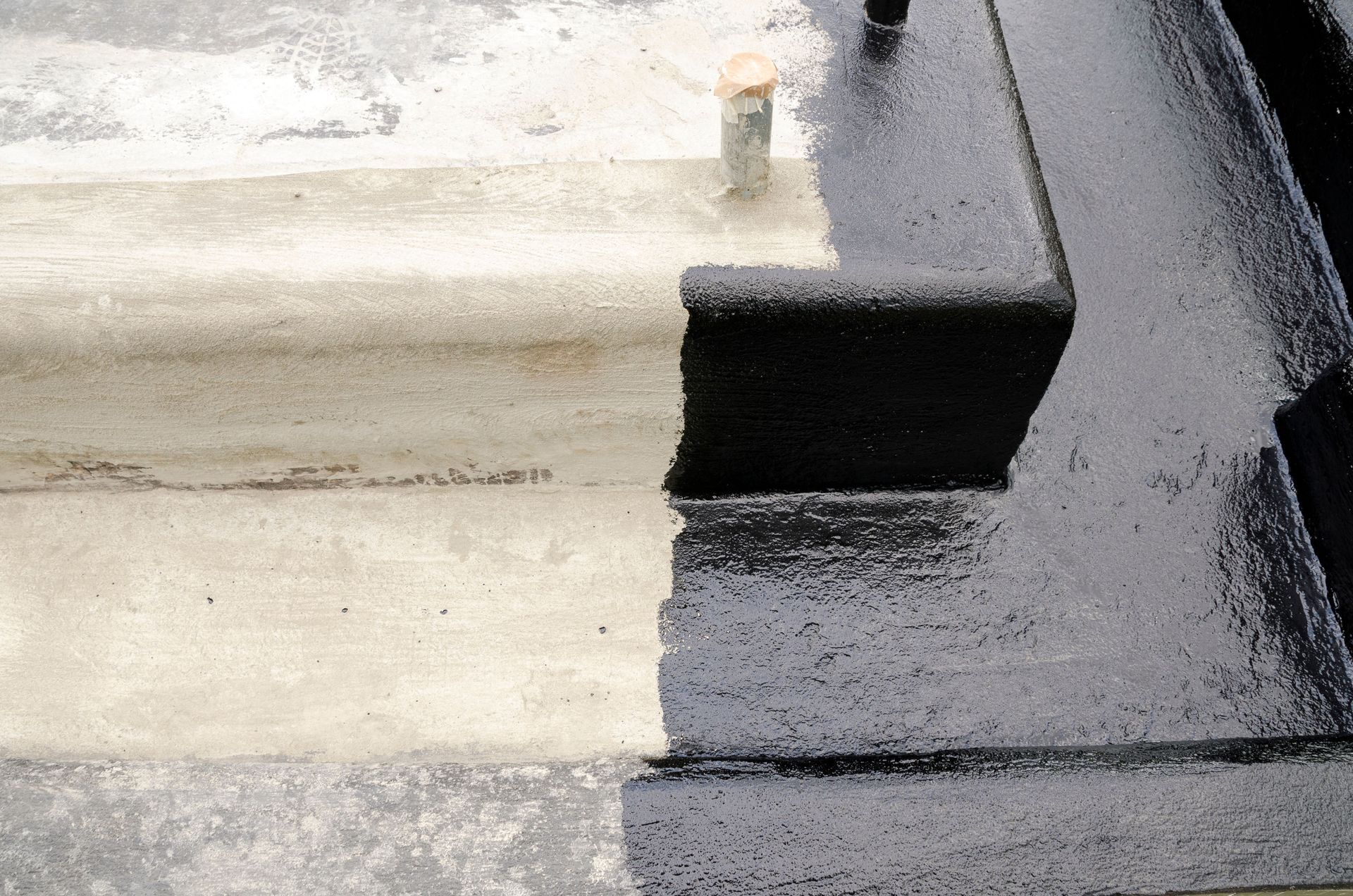 Close-up of a black-and-white rooftop corner with a small vent pipe and wet, textured surfaces