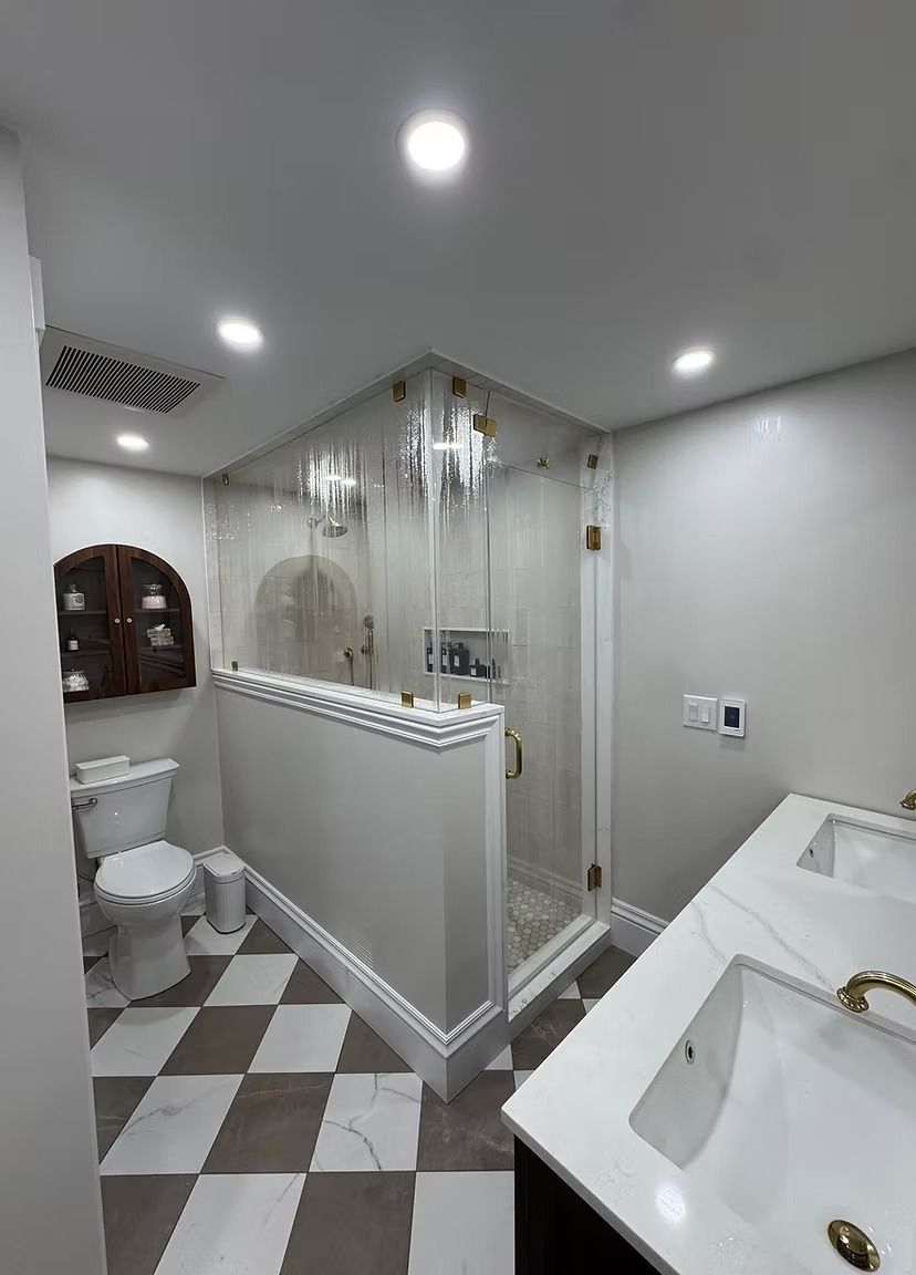 A modern bathroom with a double vanity, a glass-enclosed shower, a toilet, and brown and white diamond-patterned tile.