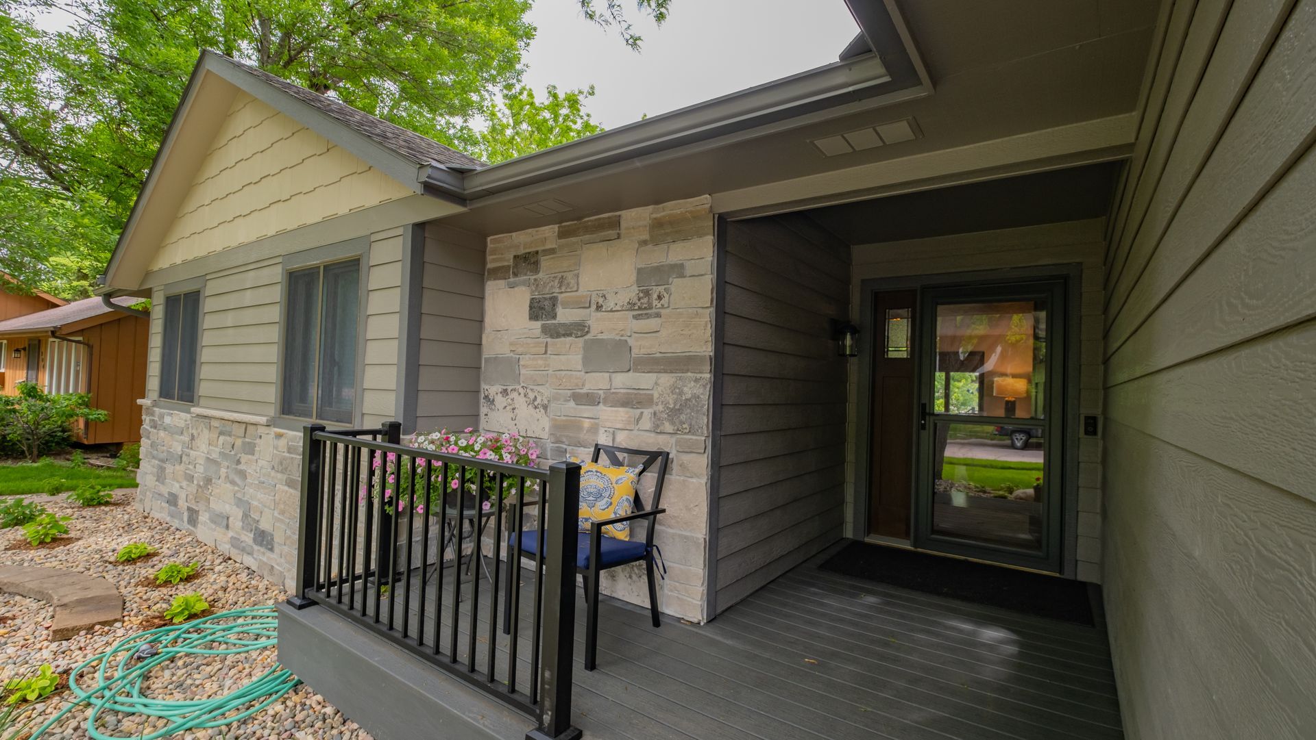 The front porch of a house with a chair and a hose.